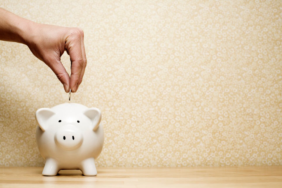 Hand dropping coin into white piggy bank