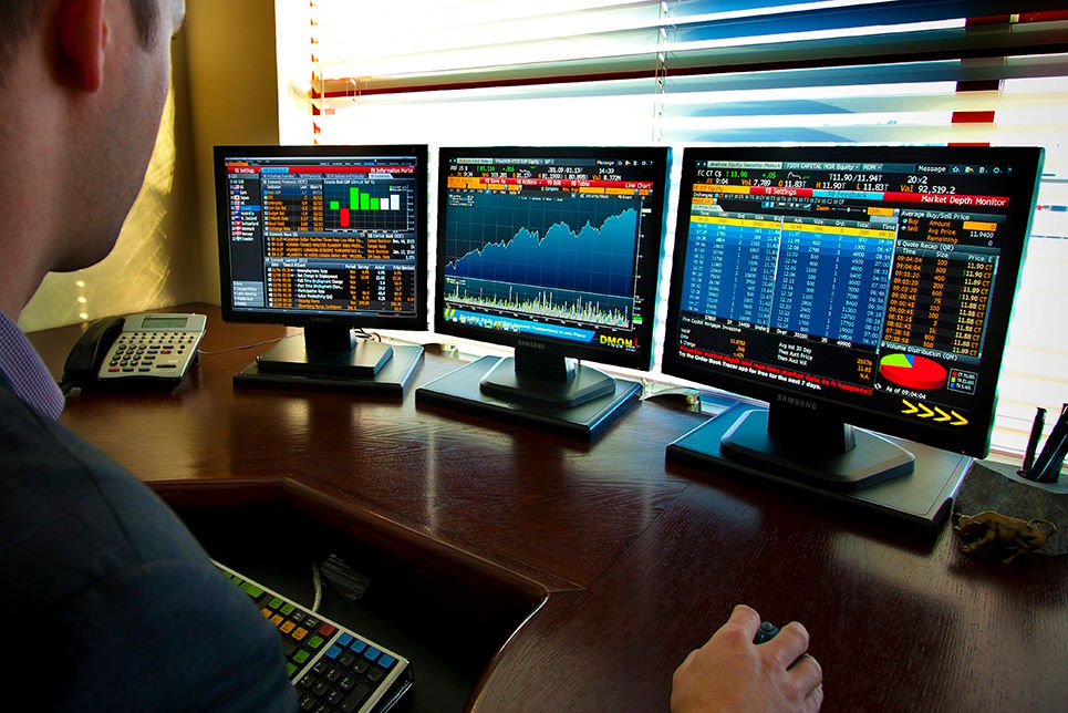Day trader looking at three monitors of stock data