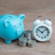 Cute blue piggy bank, a stack of coins, and a clock